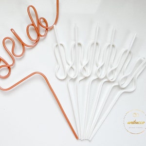 May include: A set of 10 white and one rose gold bendable straws. The rose gold straw is shaped to spell out the word "bride".