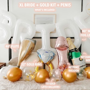 Extra large white letters spelling BRIDE hang above the bed in an arch. Below the letters on the bed rests 4 large foil balloons, a large flute, a gold ring, a green champagne bottle and 10 gold chrome and confetti filled balloons