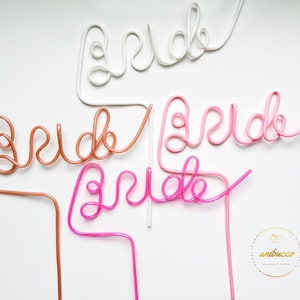 May include: Four plastic straws shaped to spell out the word "bride" in pink, white, and brown. The straws are on a white background.