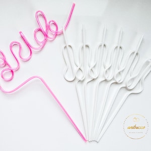 May include: Pink and white plastic straws shaped to spell "bride" and form a decorative design. The straws are on a white background.