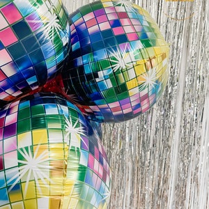 May include: Three round foil balloons featuring a multi-colored disco ball pattern with square tiles in shades of blue, green, yellow, pink, and purple. Each balloon displays white starburst accents across the surface, creating a reflective effect.