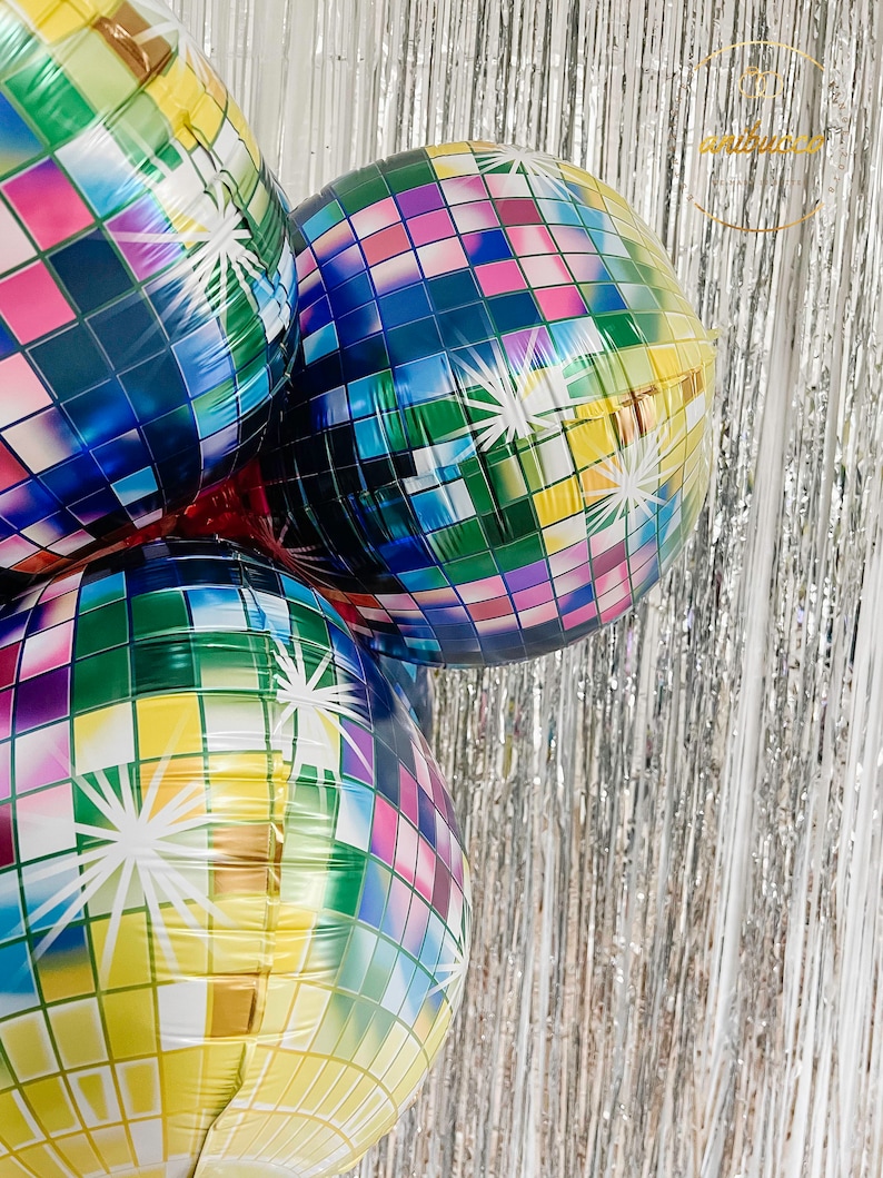 May include: Three round foil balloons featuring a multi-colored disco ball pattern with square tiles in shades of blue, green, yellow, pink, and purple. Each balloon displays white starburst accents across the surface, creating a reflective effect.