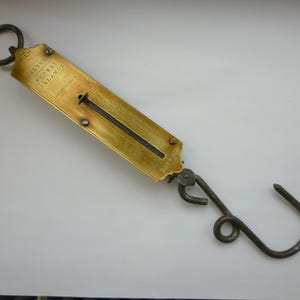 May include: Vintage brass pocket balance scale with a hook and ring. The scale is inscribed with "ALTER POCKET BALANCE" and "BRITISH MADE". The scale is gold-toned with a dark grey hook and measures in grams.