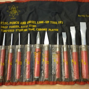 May include: A 12-piece punch and chisel line-up tool set. The tools are chrome-plated and made of alloy steel. The set is in a black and red tool roll with the text "TOOL STAR JAPAN".