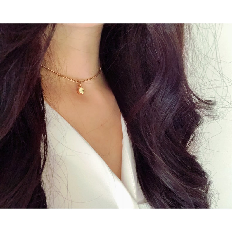 Collar with shiny pendant encrusted with a green stone mounted on a thin gold metal chain