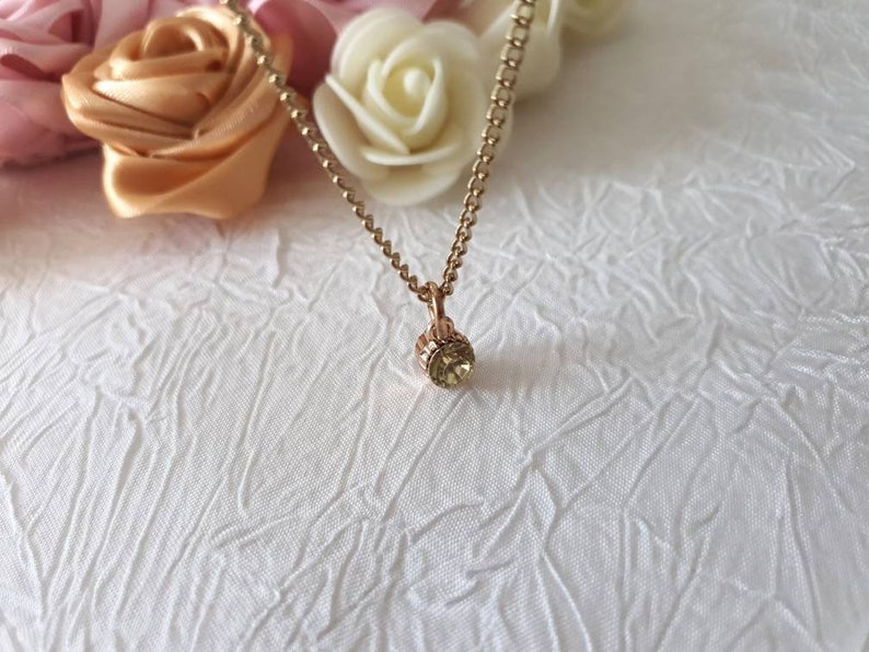 Collar with shiny pendant encrusted with a green stone mounted on a thin gold metal chain