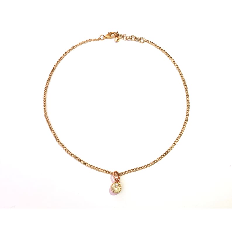 Collar with shiny pendant encrusted with a green stone mounted on a thin gold metal chain