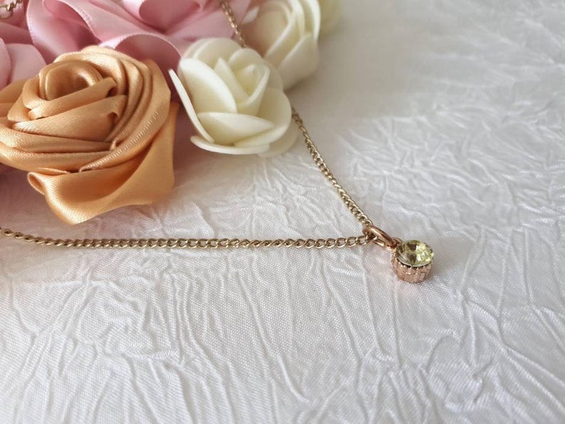Collar with shiny pendant encrusted with a green stone mounted on a thin gold metal chain