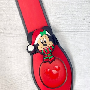 Puede incluir: Pulsera roja y negra con temática de Mickey Mouse con un amuleto de Minnie Mouse con temática navideña. El amuleto presenta a Minnie Mouse con un gorro de Papá Noel rojo, un lazo verde y una bufanda a rayas rojas y verdes.