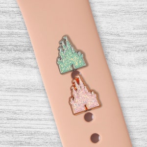 May include: Two glitter-covered Cinderella Castle charms in pink and green. The charms are attached to a pink silicone watch band.