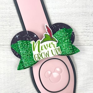 May include: Green glitter bow with a black and white starry background. The bow has a white text overlay that says "Never Grow Up!" and a green felt Peter Pan hat with a red feather.