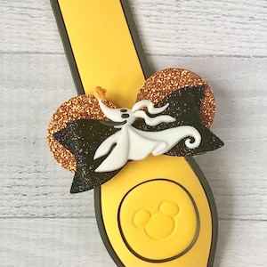 May include: A black and white Nightmare Before Christmas character bow with gold glitter accents. The bow is attached to a yellow Mickey Mouse ear headband.