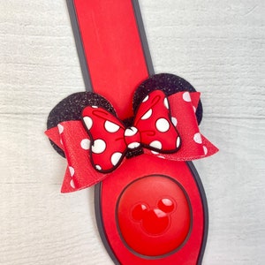 May include: Red and black Minnie Mouse ears with a white polka dot bow. The ears are attached to a red and black MagicBand.