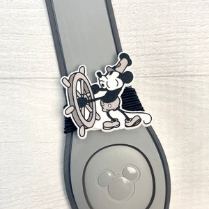 May include: A gray Mickey Mouse themed Disney park MagicBand with a black strap and a black and white Mickey Mouse character wearing a captain's hat and holding a ship's wheel.