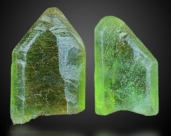 Puede incluir: Dos cristales verdes, uno con una apariencia más translúcida y el otro con una apariencia más opaca. Los cristales son ambos afilados y angulares.