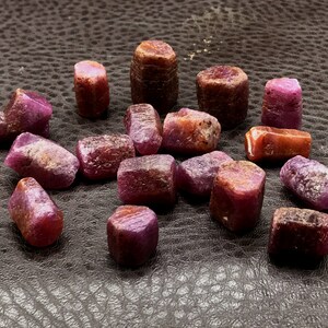 Może przedstawiać: Kolekcja 16 surowych, naturalnych rubin&oacute;w. Rubiny są w r&oacute;żnych odcieniach r&oacute;żowego i czerwonego i mają lekko nieregularny kształt.