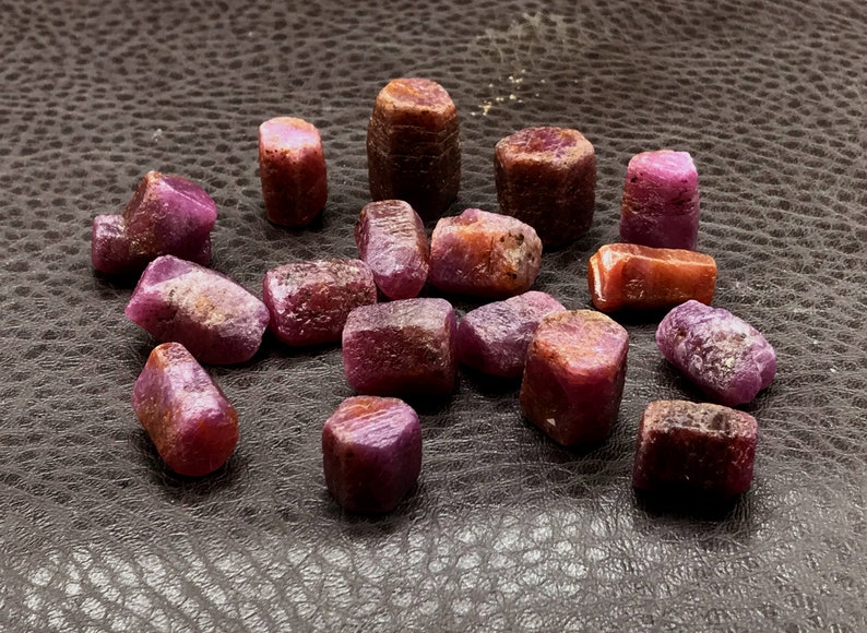 Może przedstawiać: Kolekcja 16 surowych, naturalnych rubin&oacute;w. Rubiny są w r&oacute;żnych odcieniach r&oacute;żowego i czerwonego i mają lekko nieregularny kształt.