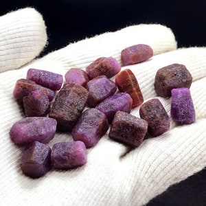 Może przedstawiać: Kolekcja surowych rubin&oacute;w w kolorze fioletowym i brązowym. Kamienie mają r&oacute;żne rozmiary i kształty oraz naturalne, nieoszlifowane wykończenie.