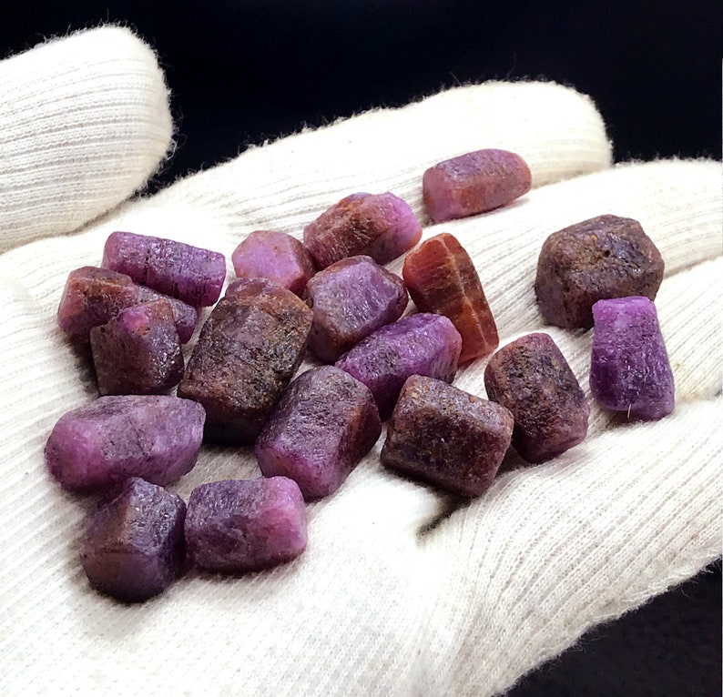 Może przedstawiać: Kolekcja surowych rubin&oacute;w w kolorze fioletowym i brązowym. Kamienie mają r&oacute;żne rozmiary i kształty oraz naturalne, nieoszlifowane wykończenie.