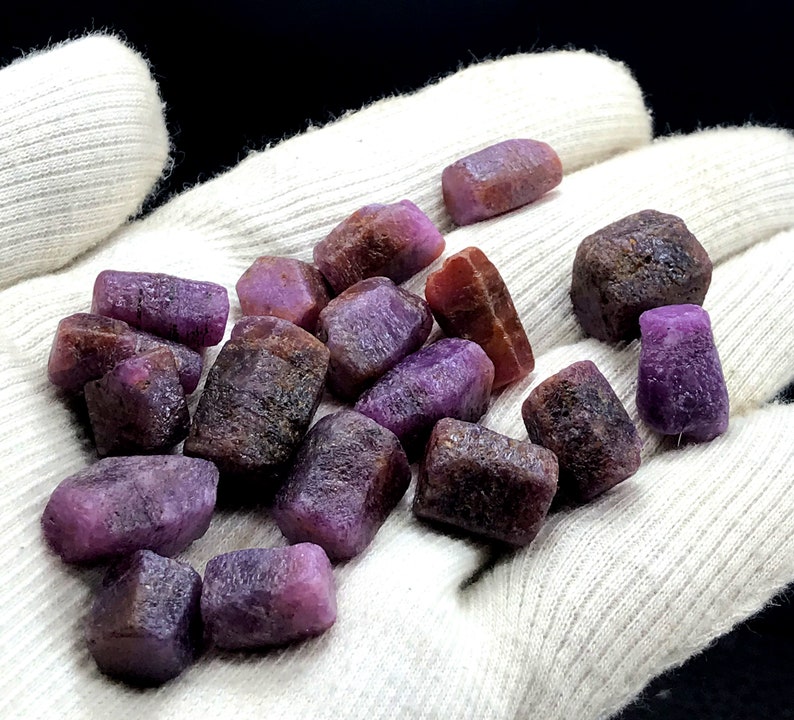 Może przedstawiać: Kolekcja surowych, fioletowych i czerwonych kamieni szlachetnych. Kamienie mają r&oacute;żne rozmiary i kształty i mają naturalne, nieoszlifowane wykończenie.