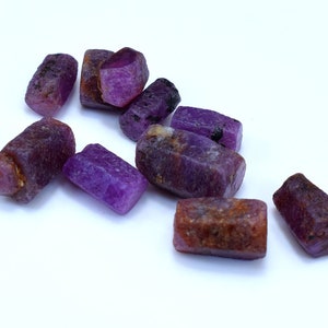 Pode incluir: Uma cole&ccedil;&atilde;o de oito gemas brutas cortadas em tons de roxo e marrom. As gemas t&ecirc;m formato retangular e um acabamento natural n&atilde;o polido.