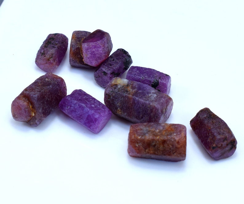 Pode incluir: Uma cole&ccedil;&atilde;o de oito gemas brutas cortadas em tons de roxo e marrom. As gemas t&ecirc;m formato retangular e um acabamento natural n&atilde;o polido.