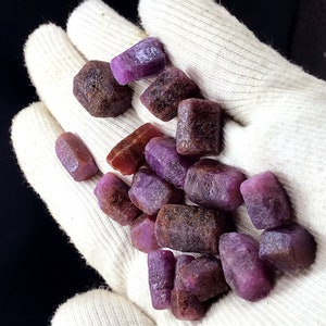 Może przedstawiać: Kolekcja surowych, fioletowych i czerwonych kamieni szlachetnych. Kamienie szlachetne są r&oacute;żnych rozmiar&oacute;w i kształt&oacute;w i mają naturalne, nieoszlifowane wykończenie.