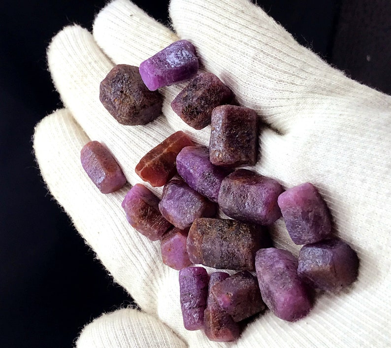 Może przedstawiać: Kolekcja surowych, fioletowych i czerwonych kamieni szlachetnych. Kamienie szlachetne są r&oacute;żnych rozmiar&oacute;w i kształt&oacute;w i mają naturalne, nieoszlifowane wykończenie.