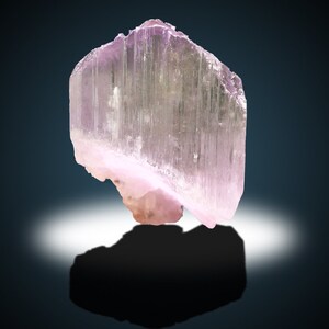 May include: A translucent pink crystal with striations, resembling a prism. The crystal has a smooth, polished surface and a slightly curved shape.