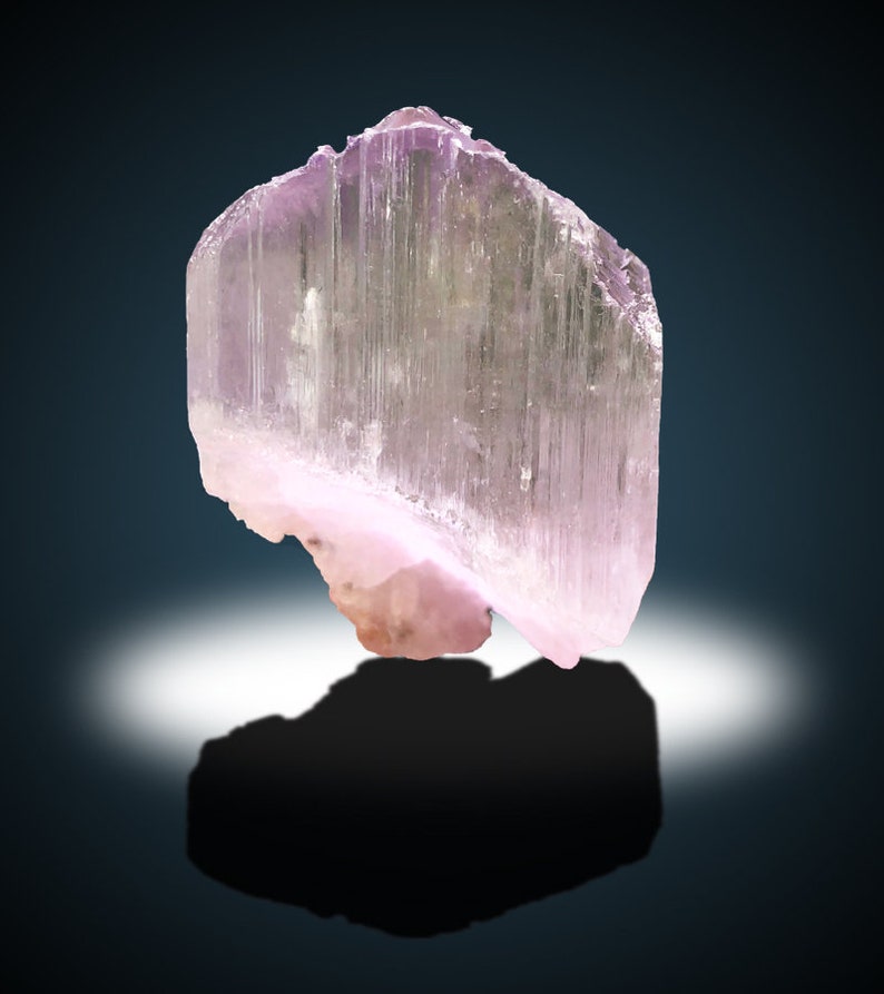 May include: A translucent pink crystal with striations, resembling a prism. The crystal has a smooth, polished surface and a slightly curved shape.