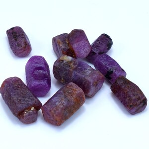 Puede incluir: Un grupo de piedras preciosas en bruto de color púrpura, probablemente rubíes, con una variedad de formas y tamaños. Las piedras tienen una textura rugosa y natural y son de un color púrpura intenso.