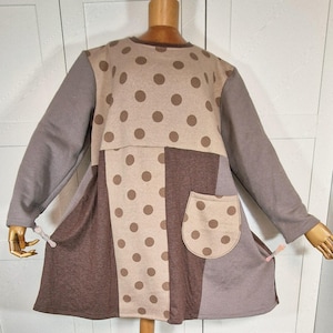 Könnte beinhalten: Ein langärmliges Tunika-Kleid in Braun-, Beige- und Grautönen mit einem Polka-Dot-Muster auf dem Oberteil und der Tasche. Das Kleid hat einen runden Ausschnitt und eine lockere Passform mit einer aufgesetzten Tasche auf der Vorderseite.