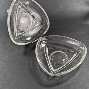 May include: A set of two clear glass triangular dishes, one nested inside the other. The dishes are made of clear glass and have a smooth, polished finish.