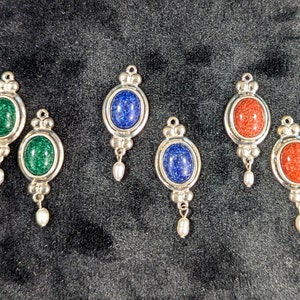 May include: Four pairs of silver dangle earrings with oval-shaped stones. The stones are green, blue, and red.