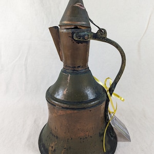 May include: An antique copper pitcher with a green patina and a hinged lid. The pitcher has a wide, bell-shaped base and a curved handle.