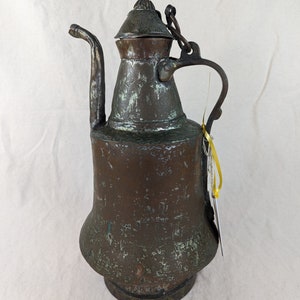 May include: An antique copper teapot with a worn green patina. The teapot has a round body with a flared spout and a hinged lid. The handle is attached to the body with a chain.