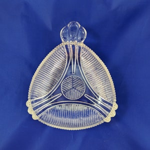 May include: A clear glass dish with a scalloped edge and a raised center design. The dish has a triangular shape and a decorative knob on the top.