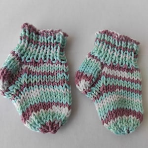 K&ouml;nnte beinhalten: Ein Paar handgestrickte Babyschuhe mit einem mehrfarbigen Garnmuster in den T&ouml;nen Hellgr&uuml;n, Wei&szlig; und gedecktem Violett. Die Schuhe haben ein geripptes B&uuml;ndchen am oberen Rand und einen abgerundeten Zehenbereich, gefertigt im gleichm&auml;&szlig;igen Strickmuster.