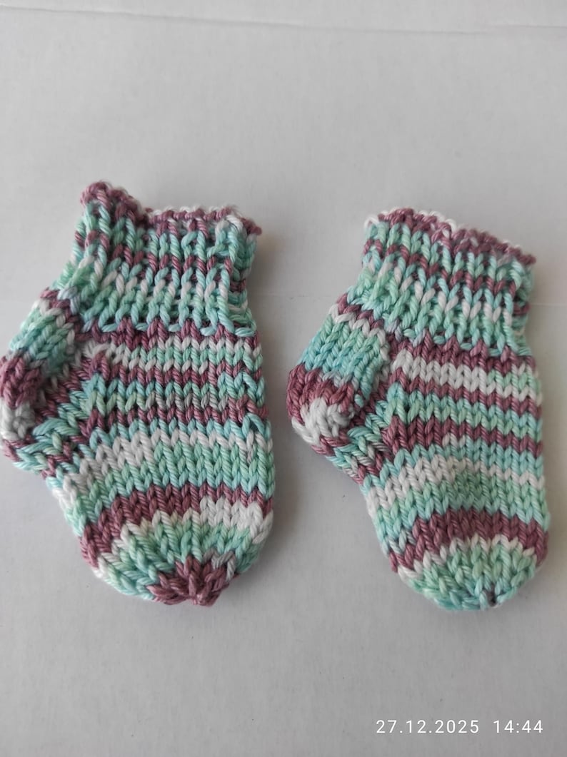 K&ouml;nnte beinhalten: Ein Paar handgestrickte Babyschuhe mit einem mehrfarbigen Garnmuster in den T&ouml;nen Hellgr&uuml;n, Wei&szlig; und gedecktem Violett. Die Schuhe haben ein geripptes B&uuml;ndchen am oberen Rand und einen abgerundeten Zehenbereich, gefertigt im gleichm&auml;&szlig;igen Strickmuster.