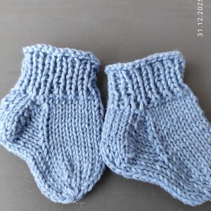 K&ouml;nnte beinhalten: Ein Paar hellblaue gestrickte Babyschuhe mit geripptem B&uuml;ndchen und einem glatt rechts gestrickten Fu&szlig;teil. Die Schuhe haben eine ausgepr&auml;gte Fersenkonstruktion und eine abgerundete Zehenpartie, gefertigt aus weichem Garn mit Struktur.