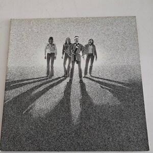 May include: Black and white photograph of a four-piece band standing in a line. The men are wearing casual clothing and looking at the camera. The photo was taken in a studio setting with a plain white background.