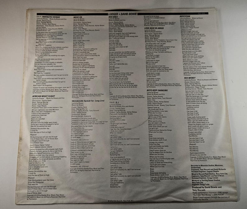 May include: A vintage vinyl record album cover featuring song lyrics and credits. The cover is off-white with black text, showcasing the album's tracklist and artist information. The album is by Lodger and David Bowie.