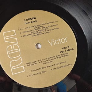 May include: A black vinyl record with a gold label featuring the album title "Lodger" by David Bowie. The label includes song titles, the RCA and Victor logos, and the text "Side B".