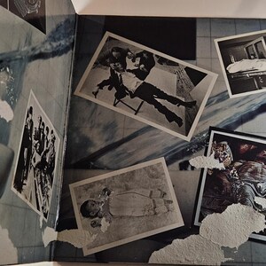 May include: An open book with a blue and white abstract design. Several black and white photographs are scattered across the pages, depicting various scenes. The photos are of different sizes and shapes.