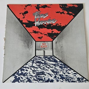 May include: A square vinyl record cover featuring the text Fates Warning in silver lettering against a red and black sky. The center shows a white sign with the text NO EXIT above a dark, textured ground, framed by two gray concrete walls.