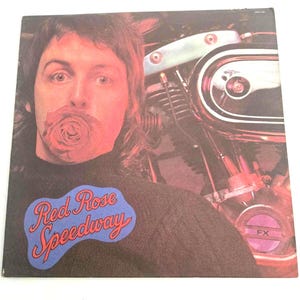 May include: A vintage vinyl record album cover featuring a man with a red rose in his mouth, a motorcycle engine in the background, and the text "Red Rose Speedway".
