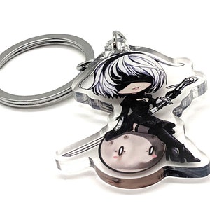 May include: A clear acrylic keychain featuring a cartoon character with white hair and a black outfit, holding a sword and sitting on a round object.