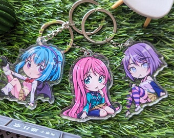 May include: Three anime character keychains with silver key rings. The keychain on the left features a blue-haired character with purple eyes and a pink and yellow outfit. The keychain in the middle features a pink-haired character with blue eyes and a green and white outfit. The keychain on the right features a purple-haired character with blue eyes and a white and purple outfit.