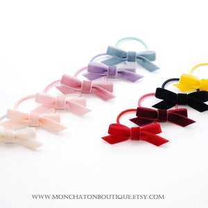 Peut inclure: Assortiment de chouchous en velours de différentes couleurs, dont le rose, le violet, le bleu, le noir, le rouge et le jaune. Chaque chouchou est orné d'un petit nœud.