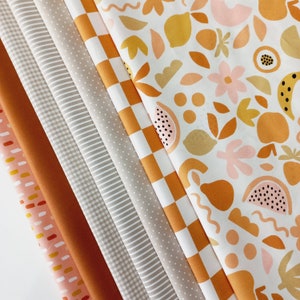 Könnte beinhalten: Eine Sammlung von acht Stoffproben in verschiedenen Mustern und Farben, darunter Orange, Braun, Beige und Weiß. Die Muster umfassen Gingham, Punkte, Streifen und ein geometrisches Design. Die Stoffproben sind fächerförmig angeordnet.